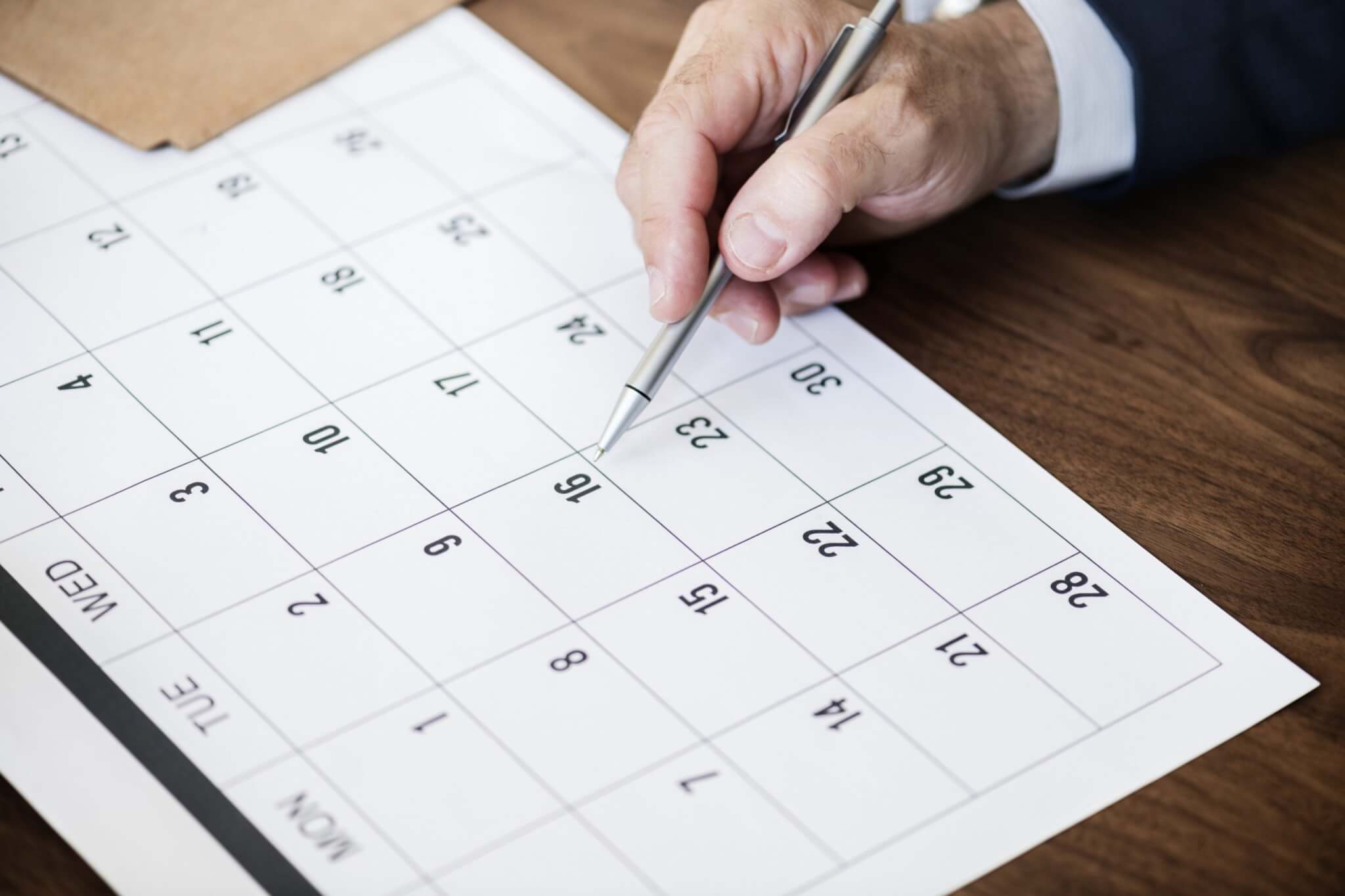 a person holding a pen over a calendar