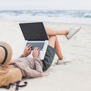 a woman lying on the beach using a laptop