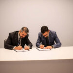 two men sitting at a table signing papers
